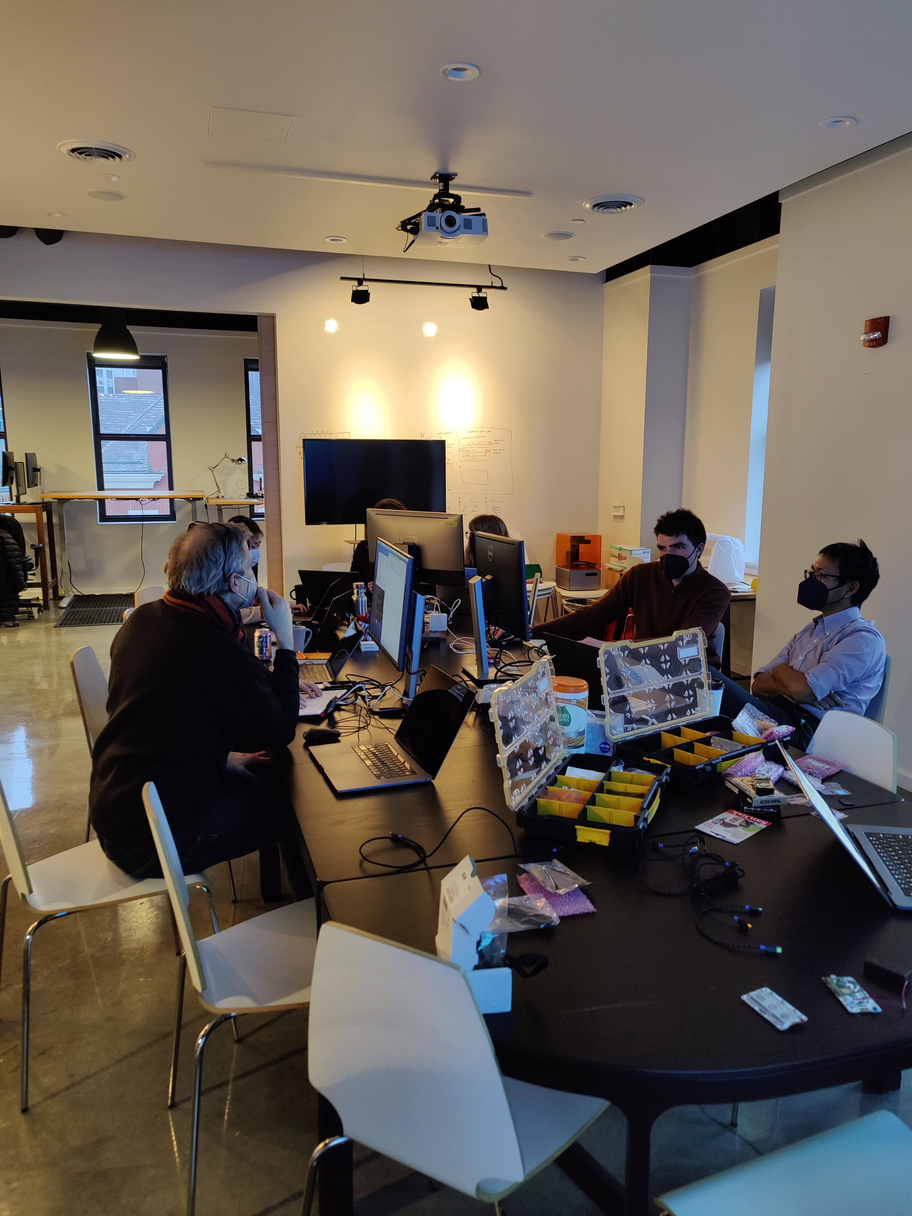 Fathom team members sitting around the conference table, surrounded by laptops, monitors, and all sorts of hardware bits and bobs.