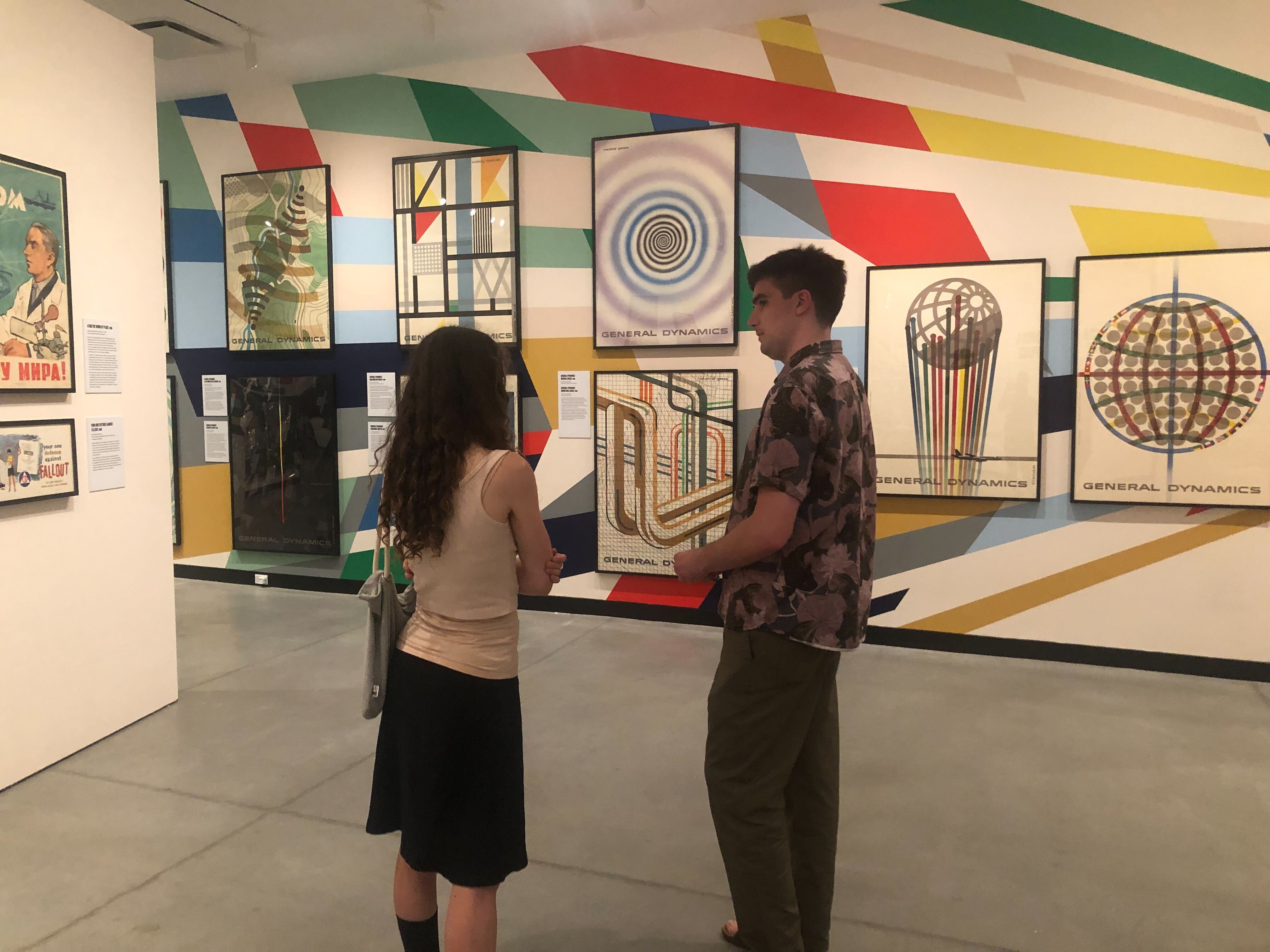 Paul and Libby talking to each other and viewing the posters on display in one of the galleries at the Poster House museum.
